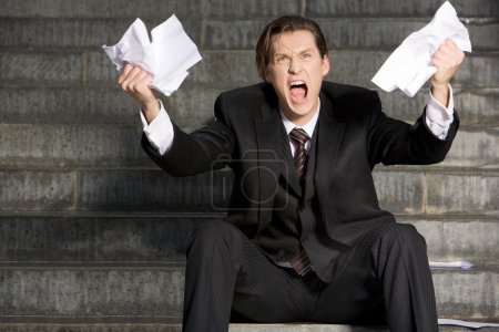 Photo of screaming businessman with two sheets of paper in his hands