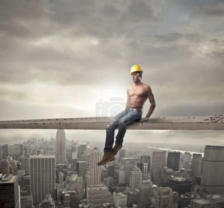 Young brawny worker sitting on a metal bar over a big city
