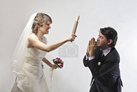 Angry bride waving threateningly a rolling pin against her husband