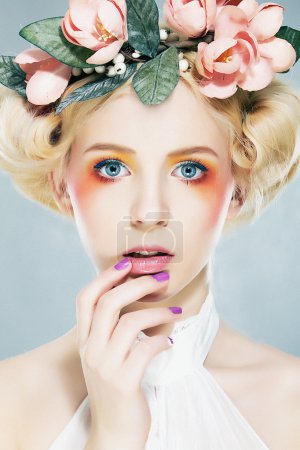 Beautiful blonde supermodel in wreath of flowers studio shot
