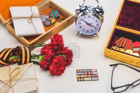 closeup shot of alarm clock, eyeglasses, flowers wrapped by st. george ribbon, letters, medals on gray, victory day concept