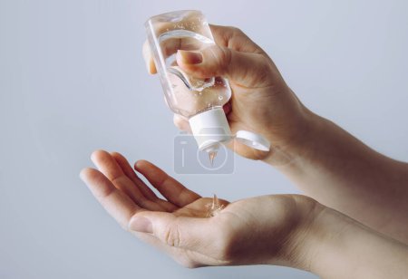 Close up view of woman person using small portable antibacterial hand sanitizer on hands.