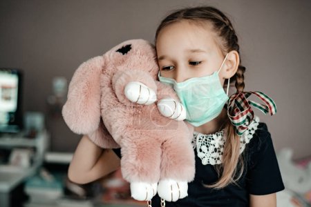little girl in medical mask holding toy, protected from corona virus