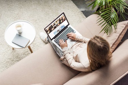 high angle view of woman at home sitting on couch and using laptop with shutterstock homepage on screen
