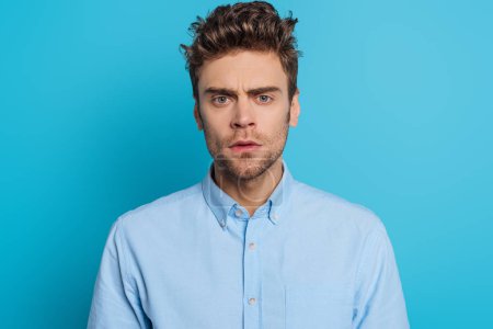 serious, thoughtful young man looking at camera on blue background