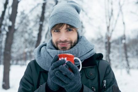 young man holding cup of hot coffee in hands in winter park