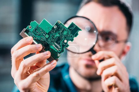 Close-up view of man looking at circuit board through magnifying glass