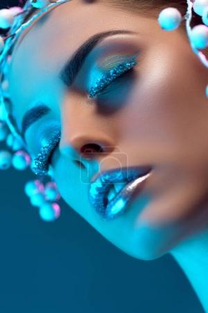 attractive woman with hair accessory, winter makeup and glitter posing for fashion shoot, isolated on blue
