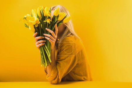 young woman holding beautiful yellow spring flowers on yellow 