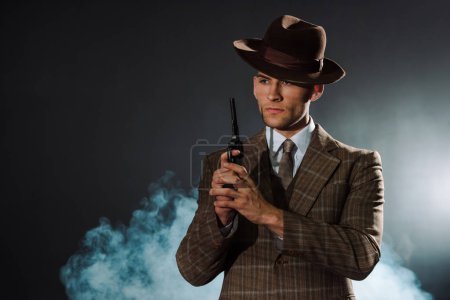 handsome man in siot and hat holding gun on black with smoke 