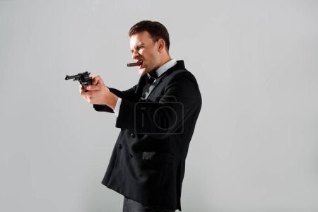 handsome gangster holding gun while smoking isolated on grey 