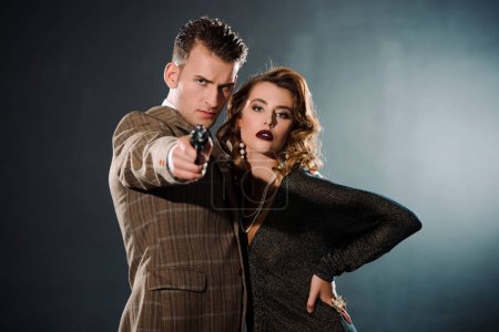 selective focus of dangerous gangster holding gun and standing near attractive woman  on black 