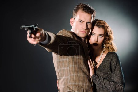 attractive woman standing near armed gangster with gun on black 