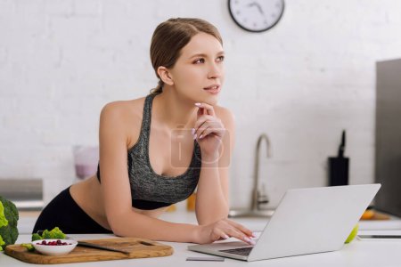 pensive girl near credit card and laptop in kitchen  
