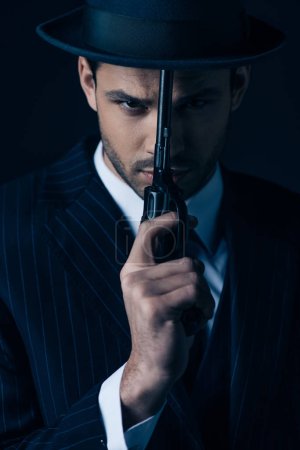 Gangster holding gun in front of face on dark blue