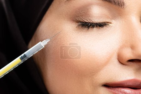 close up view of young Muslim woman in hijab with closed eyes having beauty injection
