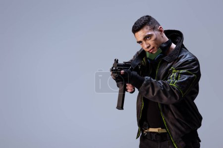 handsome bi-racial cyberpunk player holding gun isolated on grey  