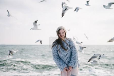 attractive smiling girl posing on winter seashore with seagulls