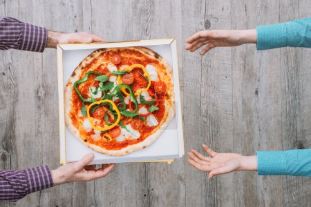 Pizza delivery at home: a man is handing a pizza in a box to a woman