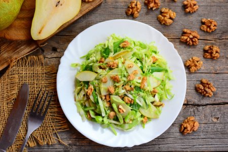 Cabbage and pear slaw recipe. Healthy salad with raw pear, cabbage and walnuts on a plate. Rustic wooden background. Clean eating diet. Closeup. Top view. Raw food diet. Raw food diet weight loss