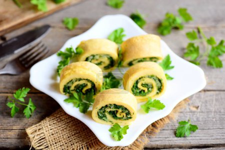 Appetizing omelette rolls with cheese and greens on a white plate and a vintage wooden table. Stuffed sliced omelette recipe idea. Country style