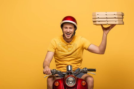 smiling delivery man in yellow uniform riding scooter with pizza boxes isolated on yellow