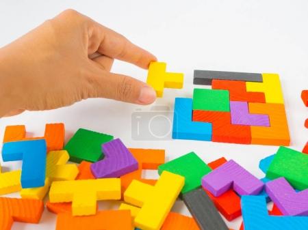 hand holding the last piece to complete a square tangram puzzle colorful wooden puzzle for kid on white background