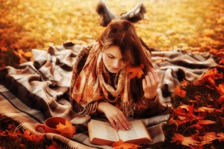 Beautiful young brunette sitting on a fallen autumn leaves in a 