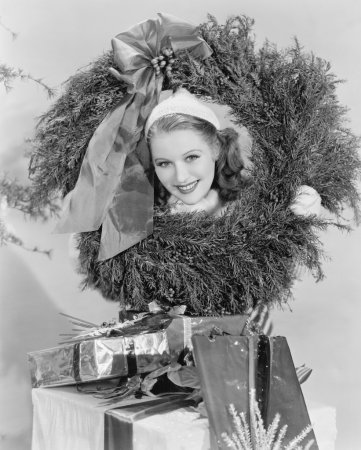 Young woman looking through a wreath with presents in front of her