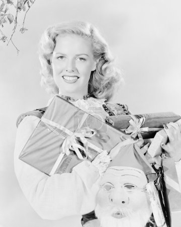 Young woman holding an arm full of presents and a Santa Claus mask