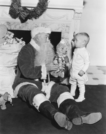 Santa Claus with a little boy and a teddy bear in front of a fire place