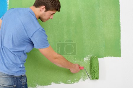 Handsome young man paint white wall in color