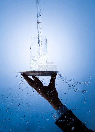 Image of waiters hand holding tray with glass on it being poured with pure water