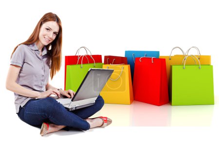 Young beautiful woman using a laptop for online shopping with 3d shopping bags in the background