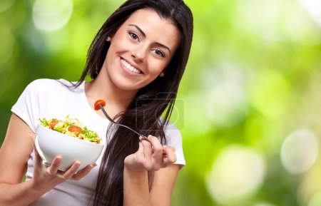 Portrait of healthy woman eating salad against a nature backgrou