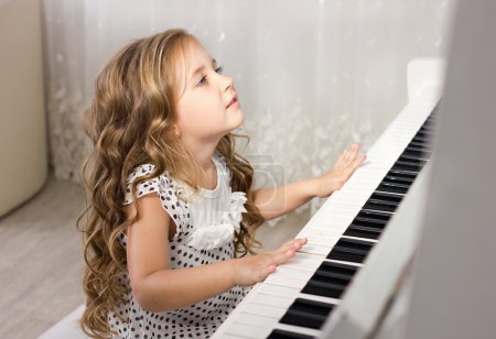 Beautiful blond little girl learn from playing near a piano