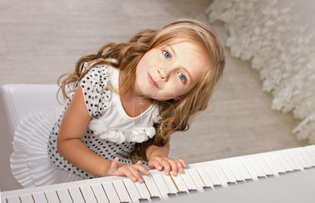 Beautiful blond little girl in pretties sitting near a piano